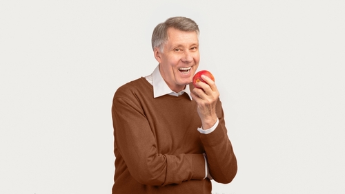 Older man laughing and holding an apple with a confident smile