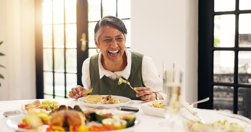 Smiling older woman laughing at a dinner table at home